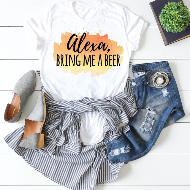 Alexa Bring Me Beer Sublimation Transfer on a white t-shirt, with casual outfit including distressed jeans, gray shoes, and accessories, laid out on a white wooden background with a potted plant and a notebook.
