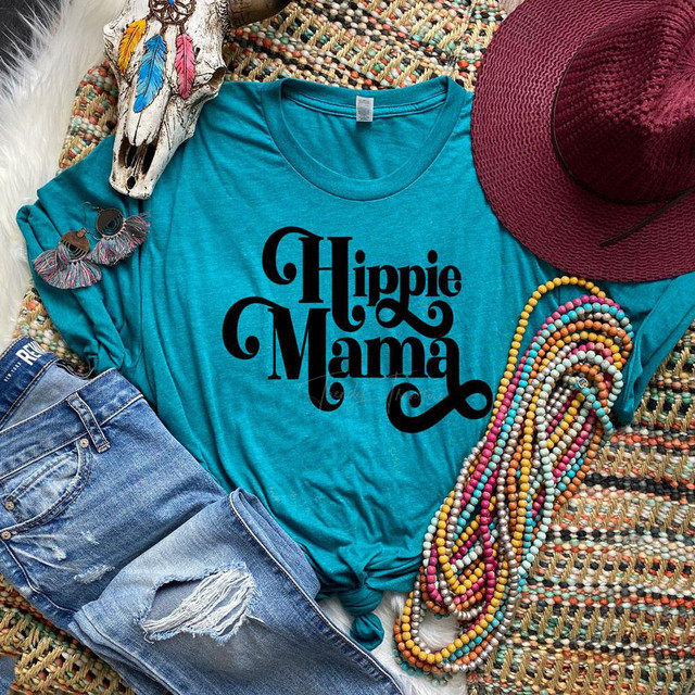 Hippie Mama Screen Print Heat Transfer, turquoise t-shirt with Halloween-inspired typographic design, surrounded by colorful accessories including beads, a maroon hat, earrings, and decorative feathers.