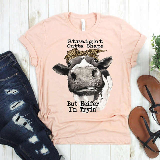 Product: Straight Outta Shape But Heifer I'm Tryin' Screen Print Heat Transfer T-shirt, pink t-shirt with a graphic of a cow wearing a leopard print bandana, featuring humorous text about being out of shape and trying.