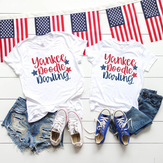 Yankee Doodle Darling Family Set Sublimation Transfer, two white T-shirts with patriotic red and blue text and star design for family matching shirts, paired with denim shorts and sneakers, displayed with American flag-themed bunting.