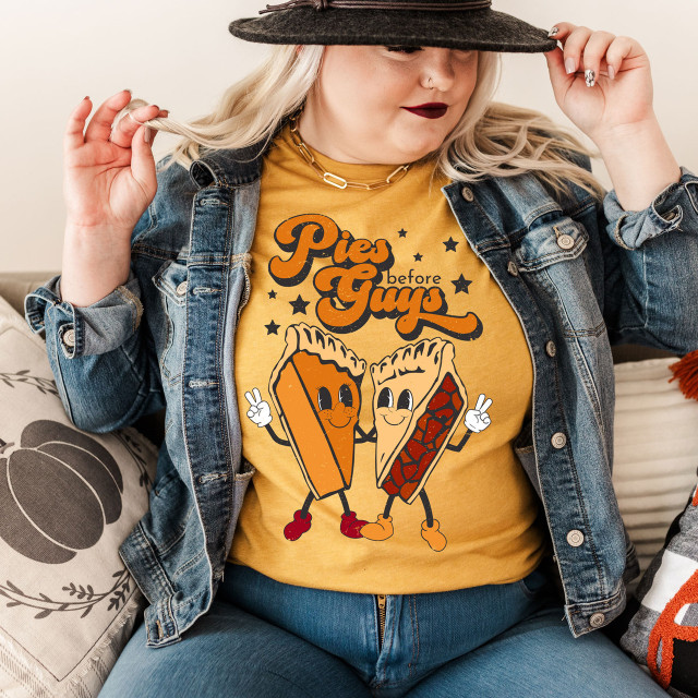 Pies Before Guys Screen Print Heat Transfer, woman wearing a yellow T-shirt with cartoon pies holding hands and text, denim jacket, sitting on a sofa.