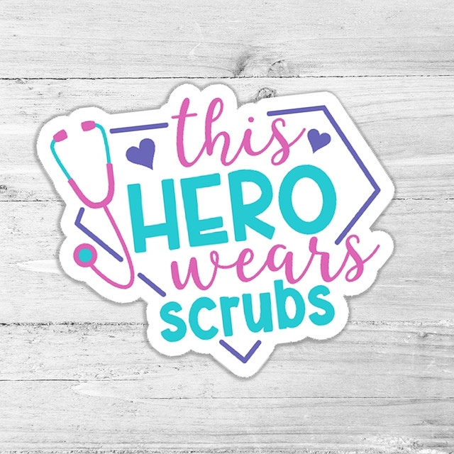 This Hero Wears Scrubs Die Cut Sticker, colorful sticker with medical theme saying "this hero wears scrubs" along with a stethoscope illustration on a white wooden background.