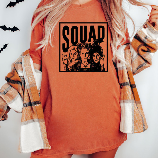 Squad Witches DTF Transfer, Halloween themed graphic on a woman's orange t-shirt with images of witches and the word 'SQUAD' in bold black letters.