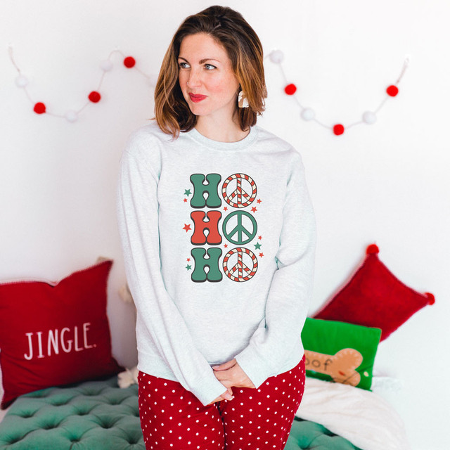 Ho Ho Ho Peace Sign Screen Print Heat Transfer, a festive holiday shirt with green and red holiday-themed lettering and icons on a woman in Christmas pajamas.
