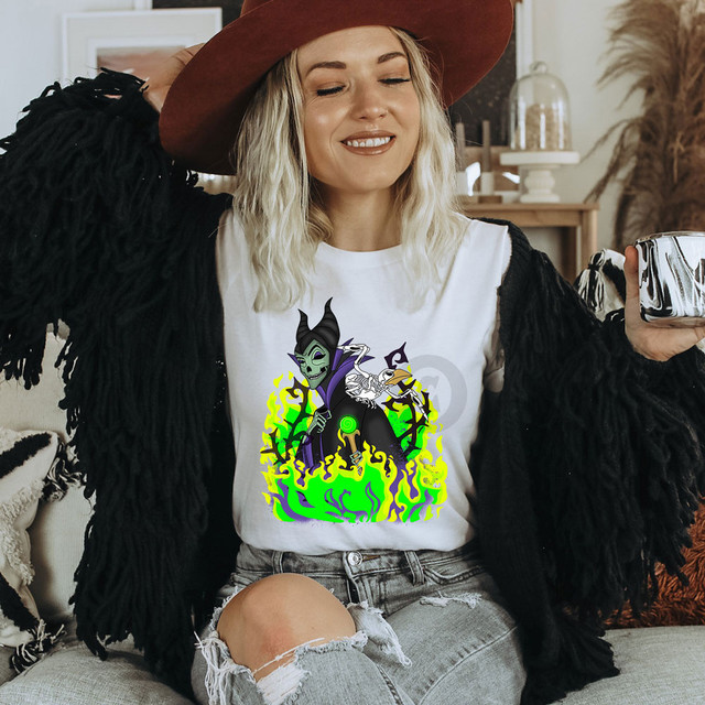 Skellie Mal DTF Transfer, a woman wearing a Halloween themed T-shirt featuring a cartoon witch with a skull face and bones, surrounded by green flames.