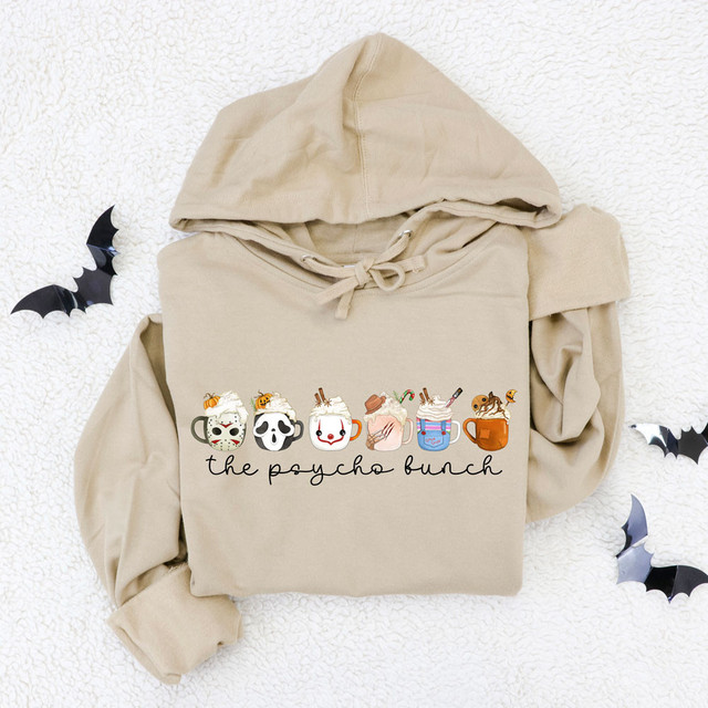 The Psycho Bunch Screen Print Heat Transfer, trendy beige hoodie with Halloween-themed mug designs, including spooky and cute characters, on a textured white background with decorative bats.