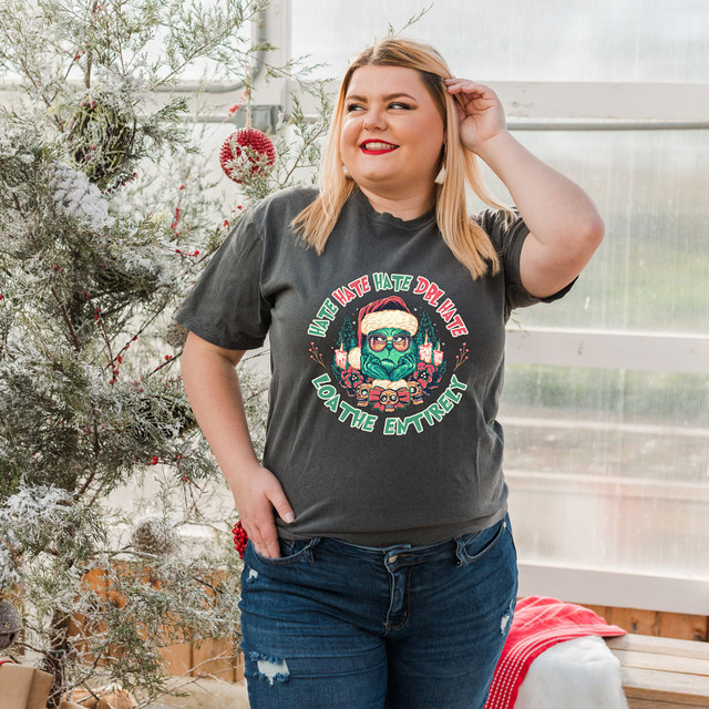 Loathe Entirely Screen Print Heat Transfer, a woman wearing a dark gray T-shirt with a colorful graphic design and humorous text, standing in a festive, winter-themed setting.