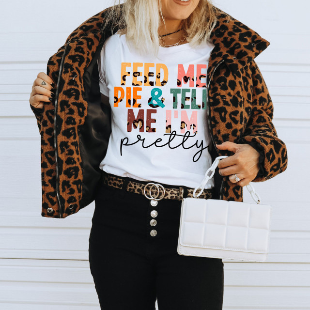 Feed Me Pie and Tell Me I'm Pretty DTF T-Shirt, woman wearing a colorful graphic tee with leopard print jacket, holding a white handbag against a white background.