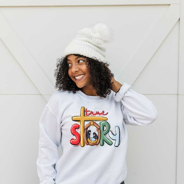 Watercolor True Story DTF Transfer, colorful watercolor design of the words 'true story' with penguin and house graphics on a white sweatshirt worn by a smiling woman.