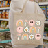 Retro Daisy DTF Heat Transfer, colorful illustrations of smiley faces, rainbows, mushrooms, and daisies on a beige tote bag.