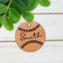 Personalized Leather Baseball Softball Keychain, round tan leather keychain with black embroidered baseball stitches and customizable name 'Smith' in black script, placed on white wooden background with green foliage.