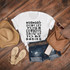 Mamas Don't Let Your Cowboys Grow Up To Be Babies Sublimation Transfer, product image of a white T-shirt with black text, paired with denim shorts, a straw hat, beige sandals, sunglasses, a brown handbag, and a polka-dotted phone case on a wooden floor.