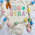 Eggstra Chenille 'look' DTF Heat Transfer on a baby onesie with pastel-colored embroidered letters and star pattern.