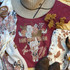 Last Night Screen Print Heat Transfer, a graphic of a cow skull with floral decorations and the text "Last Night We Let the Liquor Talk" on a maroon T-shirt, surrounded by western accessories and dry flowers.