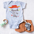 Reach for the Sky Jessie Fan Art Sublimation Transfer, a baby onesie with colorful star and cloud design featuring the phrase 'Reach for the Sky'.