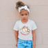 Baseball Sis DTF Heat Transfer, a young girl wearing a white t-shirt with a cute baseball-themed graphic of a smiling tooth character with a pink bow and baseball bat.