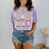 It's Okay To DTF Heat Transfer, cartoon-style colorful graphic t-shirt worn by a woman with denim shorts.