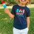 Popsicle Season DTF Heat Transfer, colorful graphic t-shirt with popsicles and text, worn by smiling child holding a red, white, and blue popsicle outdoors in a park.