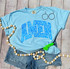 Amen NEON Blue Screen Print Heat Transfer, vibrant blue neon screen print on a light blue T-shirt with black hoop earrings and a green scrunchie, shot on a wooden surface with white and natural wood bead accessories.