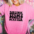 Drunk Moms Matter DTF Heat Transfer, close-up of a woman wearing a pink T-shirt with bold black text 'Drunk Moms Matter', standing against a colorful, sparkly background.