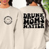 Drunk Moms Matter Happy Face DTF Heat Transfer, women wearing beige sweatshirts with printed design, one with a smiley face and the other with bold text, for custom clothing.