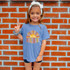 Be The Sunshine DTF Heat Transfer, colorful graphic design on a blue t-shirt worn by a smiling girl showing peace sign.