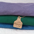 Custom Cardstock Cattle Tags, brown paper tags attached to folded colorful T-shirts in purple, green, and blue.