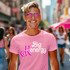 Big Kenergy DTF Heat Transfer, woman wearing pink T-shirt with Big Kenergy logo in pink and white, outdoor street scene with people and pink umbrellas.