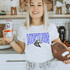 Mustangs *CUSTOM COLOR OPTIONS* DTF Heat Transfer, woman holding a can of iced tea and a football, wearing a white T-shirt with a Mustang logo and text, in a modern kitchen setting.