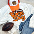 Orange Game Day Football Chenille Patch, close-up of the embroidered patch on a white sweatshirt, with a white and orange cap, jeans, a football, and jewelry surrounding it.