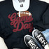 Maroon Game Day Football Chenille Patch, close-up of a football-shaped chenille patch on a black sweatshirt, with 'Game Day' text in red and black sneakers at the bottom.