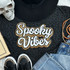 Spooky Vibes Sequins and Chenille Patch, decorative patch with the phrase 'Spooky Vibes' in white sequins outlined with gold and black beads, on a black fabric background with fashion accessories.