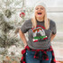 Rolling Up Some Holiday Cheer DTF Heat Transfer, a woman in a holiday-themed setting wearing a gray t-shirt with festive Christmas graphics and text, celebrating holiday cheer.