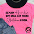 Remain Humble But Still Let These Bitches Know DTF Heat Transfer T-Shirt, pink tee with bold and cursive black text design.