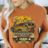 We're Running From Dinosaurs DTF Heat Transfer, vibrant graphic design on an orange T-shirt featuring dinosaurs, a Jeep with a skull, and bold lettering.