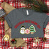 Christmas Cookie Baking Era DTF Heat Transfer, Christmas-themed design with a snowman, Christmas tree, and gingerbread cookie on a gray t-shirt surrounded by holiday decorations.