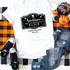 Sanderson Bed and Breakfast sublimation transfer, printed on a white T-shirt, with a black and white design featuring skulls, a pumpkin, and vintage elements, displayed alongside casual jeans, sneakers, and seasonal decorations on a plaid table runner.