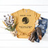 Full Moon Feelin Cute May Make Everyone Crazy Later, IDK Sublimation Transfer T-Shirt, yellow graphic tee with moon design and humorous text, displayed with denim shorts, brown shoes, and cotton bouquet on white wooden background.