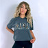 Mama Cowhide Blue DTF Heat Transfer, product image of a woman wearing a gray T-shirt with camouflage-style "MAMA" text design.