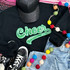 GREEN Cheer Sequin Patch, vibrant green sequined cheer logo patch on black sweatshirt, casual style with denim and sneakers, colorful felt ball string accessory, fashionable and playful visual