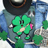 Trendy Shamrock Chenille Patch, green shamrock design with smiling face and arms holding a marshmallow skewer and pink cup, embroidered on fabric.