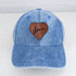 Lover Leather Hat Patch, blue denim baseball cap with a brown leather heart patch and the word 'lover' embroidered in black cursive on the patch.