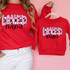 Loved Mini DTF Heat Transfer, a colorful and playful design of the phrase 'LOVED mama' on red clothing, showcasing vibrant pink and black text with decorative hearts and a striped pattern in the background.