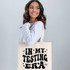 In My Testing Era DTF Heat Transfer, a woman holding a tote bag with the text 'In My Testing Era' printed on it.