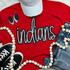Indians Sequin Patch, vibrant red t-shirt with 'Indians' written in sequins, paired with denim shorts, black sneakers, a grey cap, big earrings, and a beaded necklace.
