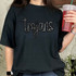 Trojans Sequin Patch, glittery black sequined patch spelling 'Trojans' on a black t-shirt worn by a woman holding a drink.