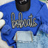 Bobcats Sequin Patch, a sparkling black and silver embroidered patch in the shape of the word 'bobcats' on a blue sweatshirt.
