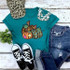 Leopard Patchwork Pumpkins Screen Print Heat Transfer, showcasing a teal t-shirt with pumpkin illustrations, paired with blue jeans, black sneakers, a leopard print cap, a white pearl necklace, and greenery on a rustic white wooden background.