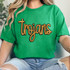 Trojans Gold Sequin Patch, a golden sequin patch spelling 'Trojans' on a green t-shirt.