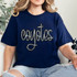 Coyotes Sequin Patch, close-up of a navy blue t-shirt featuring a sparkly sequin patch with the word 'coyotes' and a cross design, worn by a woman with blonde curly hair.